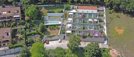 A modern multi-story residential building with a swimming pool, surrounded by lush greenery and other residential structures.