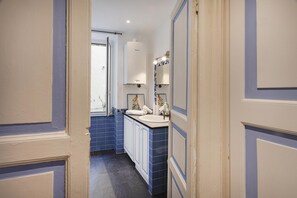 Corredor estreito que leva a um banheiro com pia branca, azulejos azuis e vaso sanitário branco.