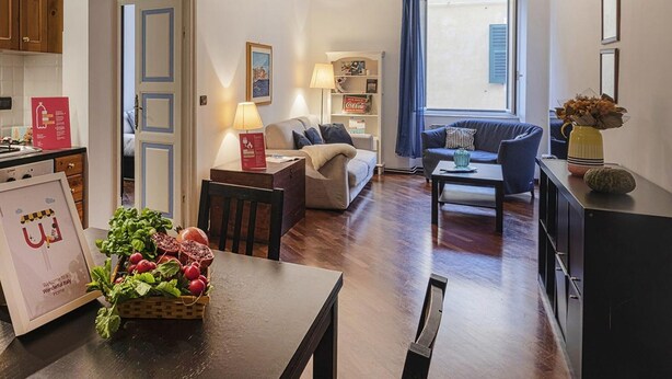 A modern living room with a sofa, a coffee table, and a dining area with a table set for a meal. - Santa Chiara Apartment by Wonderful Italy (Genoa)