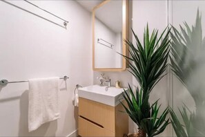 A bathroom with a white sink, wooden cabinet, towel rack, mirror, and a potted plant. - Pool, Free Carpark, Gym, Compact and Cosy Studio (South Brisbane)