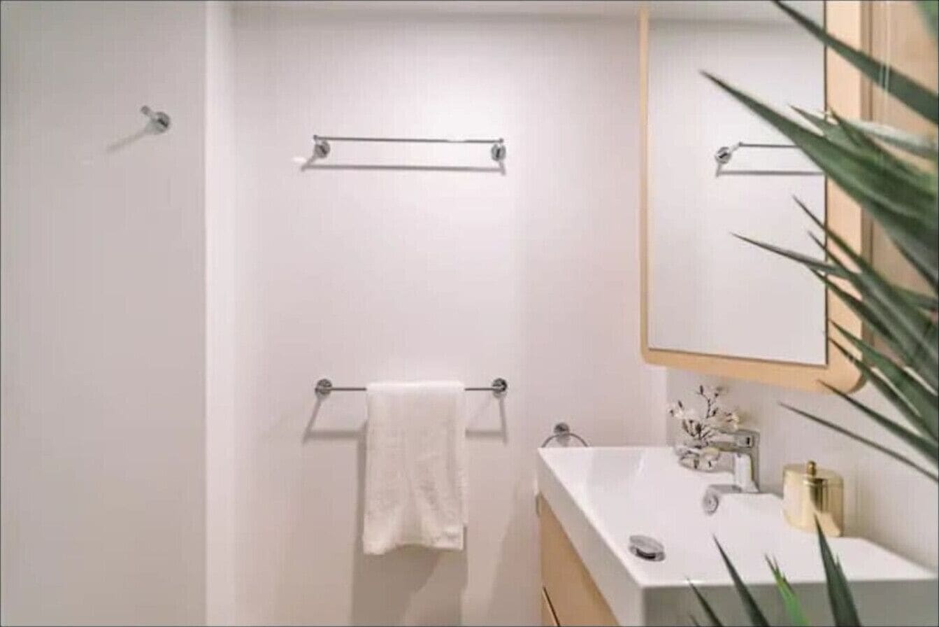 A modern bathroom with a white sink, a mirror, and a towel rack.