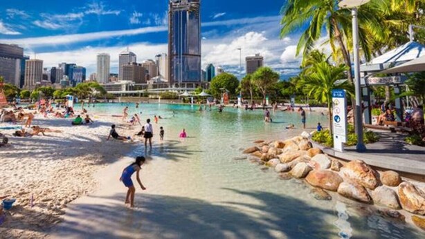 Ein Poolbereich am Strand, im Hintergrund Stadtgebäude.