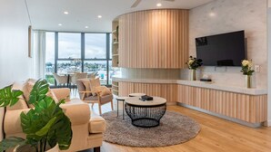 Una sala moderna con sofá, sillas, una mesita redonda, televisor y un ventanal con vista a la ciudad.