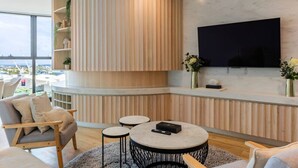 Una sala de estar moderna con una pared curva de madera, un televisor de pantalla plana montado en la pared y vistas de la ciudad a través de amplios ventanales.