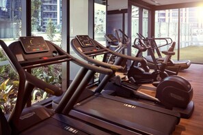 A gym with treadmills and elliptical machines, large windows, and a view of buildings outside.