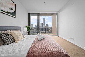 A modern hotel room with a large bed, a city view through a sliding door, and a balcony.