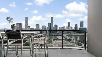A balcony with a view of a city skyline, a table with chairs, and a potted plant.