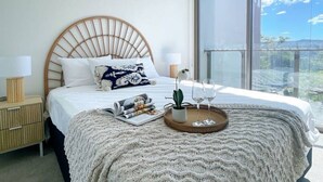 Une chambre moderne avec un grand lit, une table de chevet avec une lampe, un plateau avec des verres et une vue sur l’extérieur.