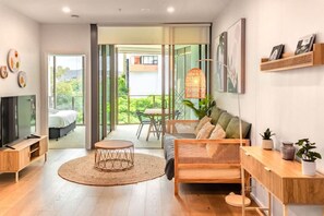 A modern living room with a TV, sofa, and dining area. - Walk to River, Cute Designer 2BR Apt in West End (West End)