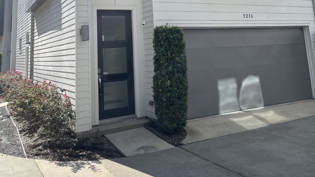 Un edificio residencial de dos pisos con balcón, garaje y un pequeño jardín.