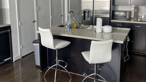 Una cocina moderna con una isla central, electrodomésticos de acero inoxidable y taburetes blancos.