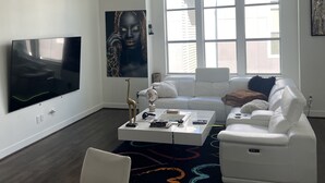 Una sala de estar moderna con un televisor de pantalla plana, sofás blancos, una mesa de centro y un ventanal grande.