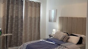 Un dormitorio moderno con una cama grande, una mesita de noche, una lámpara y una ventana con cortinas.