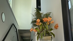 Una escalera con paredes blancas y escalones de madera oscura, que conduce a un rellano con una planta en maceta de flores naranjas.