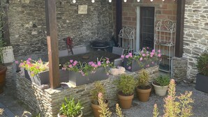A stone-walled outdoor seating area with metal chairs, potted plants, and string lights. - La Maringote 3* (Cerisy-la-Forêt)
