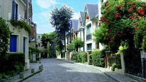 A cobblestone street lined with traditional European-style buildings, featuring balconies and lush greenery. - New architect's'apartment located in the heart of the village of Montmartre (Paris)