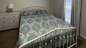 A bedroom with a bed, a nightstand, a ceiling fan, a window with curtains, and a shelf with small vases. - Cozy cottage by the lake! 18c (Phenix City)