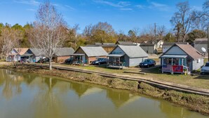 A row of small, single-story cabins with a pond in the foreground, each with a car parked in front. - Cozy cottage by the lake! 18c (Phenix City)