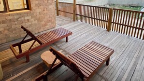 Een houten terras met twee lounge stoelen en een kleine tafel, met uitzicht op een bouwplaats met palmbomen.