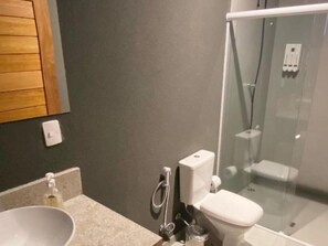 Une salle de bain avec un lavabo blanc, des toilettes et une douche fermée par des parois en verre.