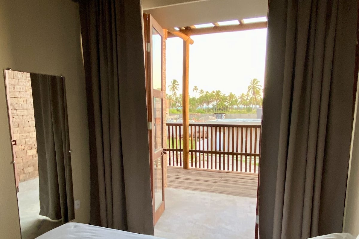 A hotel room with a bed, a view of the outdoor balcony, and a brick wall.