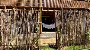 Een traditionele houten constructie met een vlechtwerk hek, een hangmat en een trap die naar een gebouw met meerdere balkons leidt.