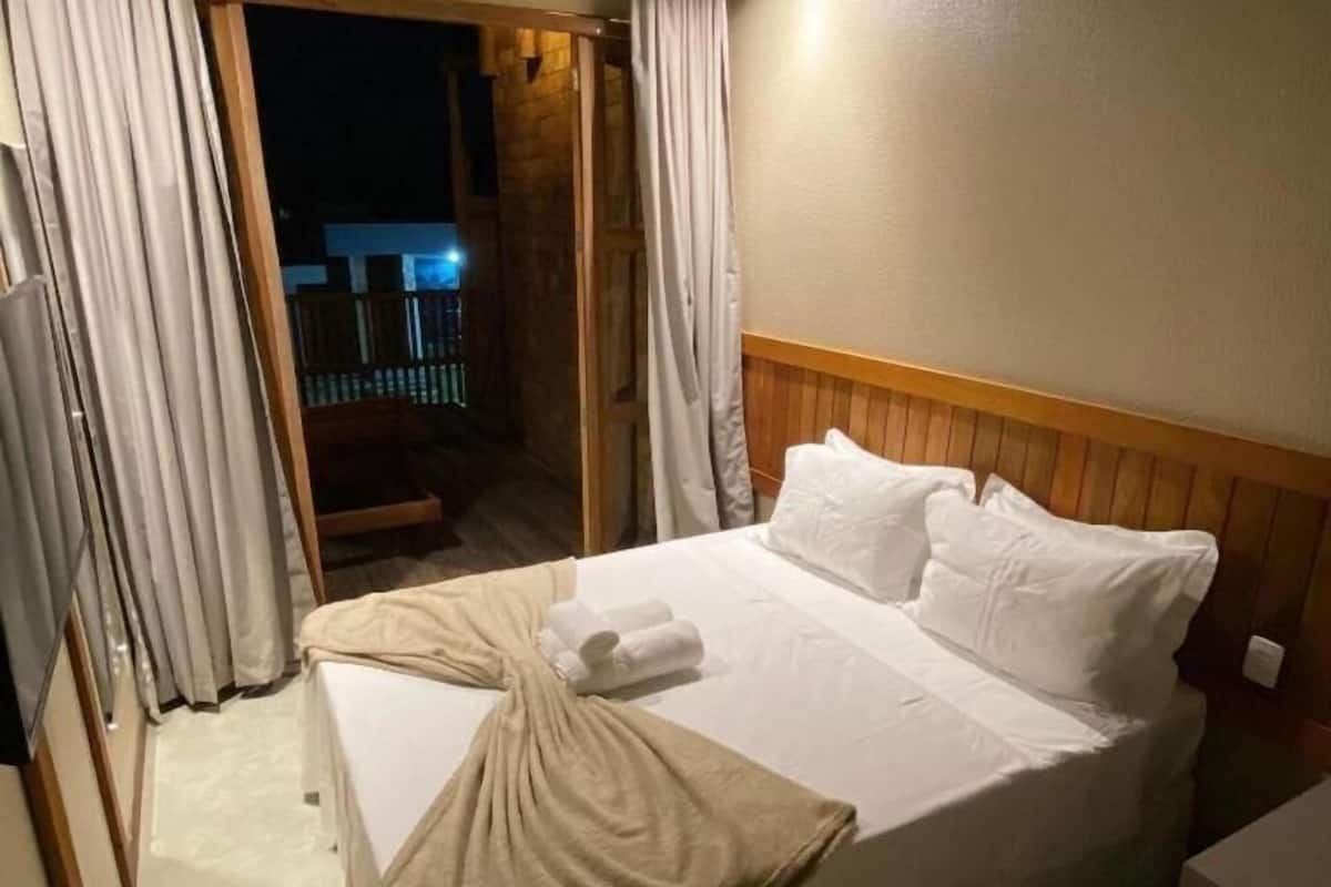 A hotel room with a bed, curtains, and a view of the outside.