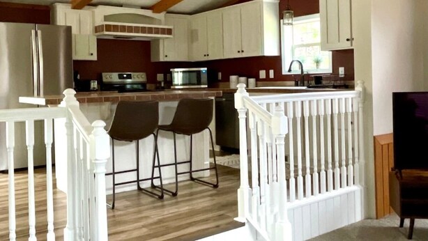 Una cocina amplia con armarios blancos, techo de madera y una zona de bar con taburetes.