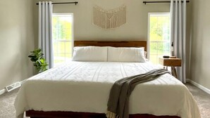 Un dormitorio con cama, ventilador de techo, un tapiz de macramé y una ventana con cortinas.