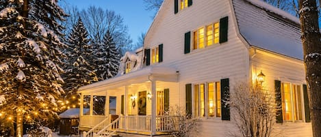 A two-story house with a porch and a covered entryway, surrounded by snow and trees.