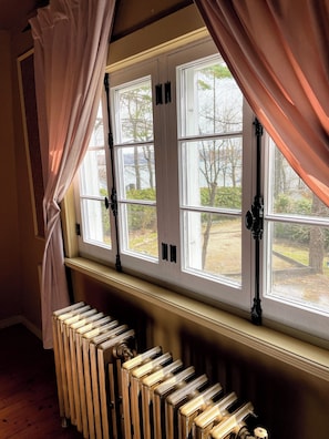 Une pièce avec un radiateur, une fenêtre à cadre blanc et des rideaux.