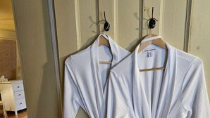 Dos batas blancas atadas a la cintura, colgadas de una puerta de madera con un ojo de cerradura.