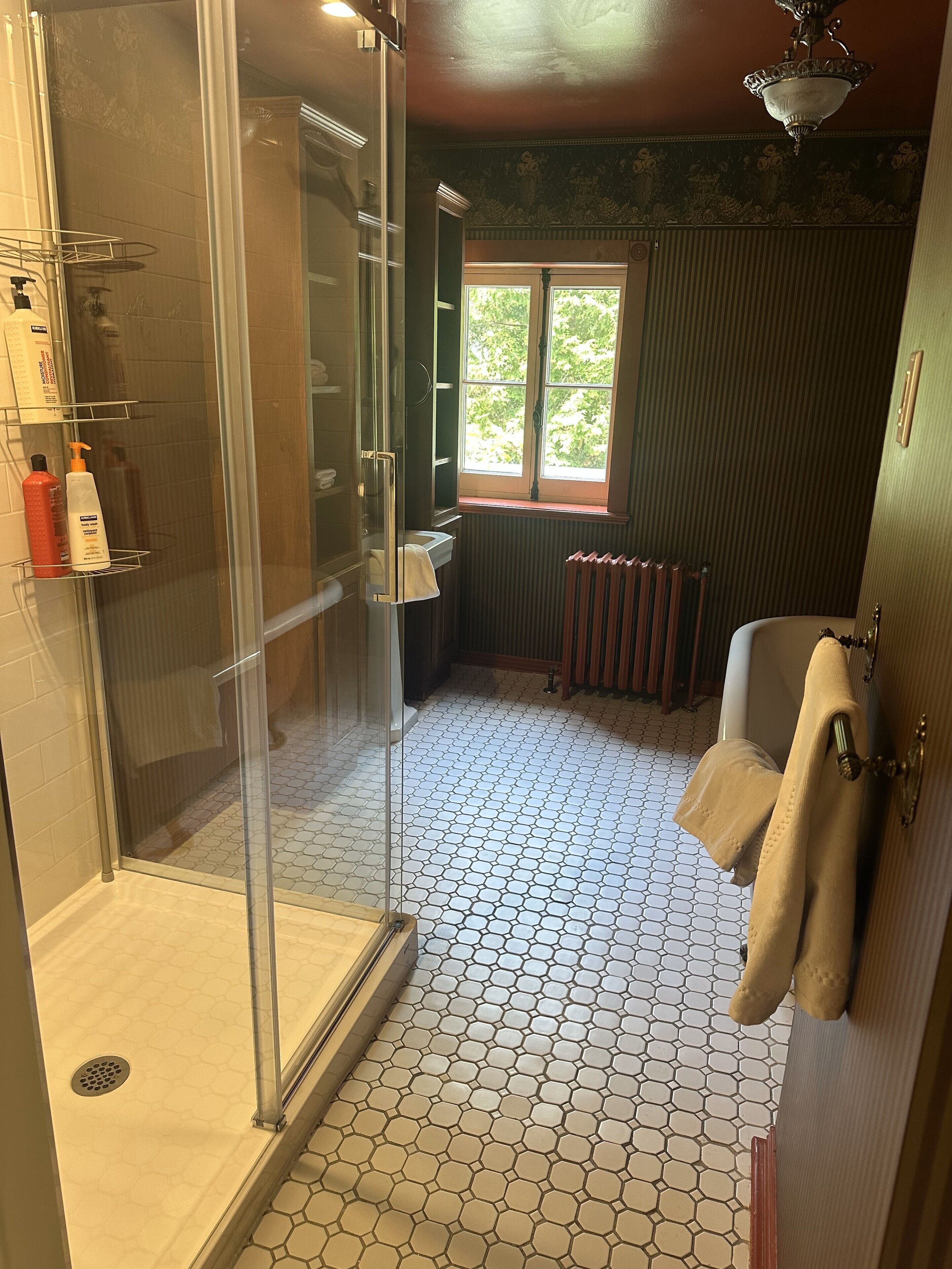 A bathroom with a glass-enclosed shower, a window providing natural light, and a radiator.