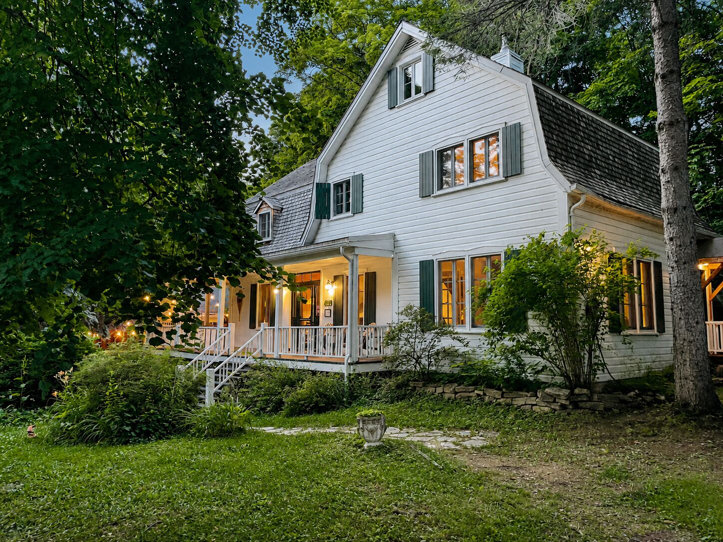 A two-story house with a porch, surrounded by greenery.