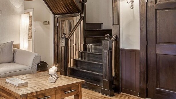 Un área de estar con piso de madera, un sofá, una mesa de centro y una escalera que conduce a una puerta de madera oscura.