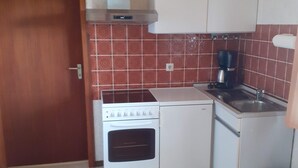 A compact kitchen with a stove, oven, sink, and white cabinets.