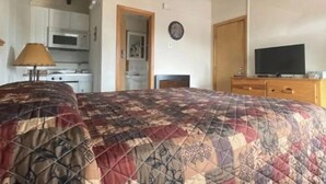 Ein Schlafzimmer mit Bett, Fernseher, einem Holzkapfen, einer Mikrowelle und einer Küchenzeile.