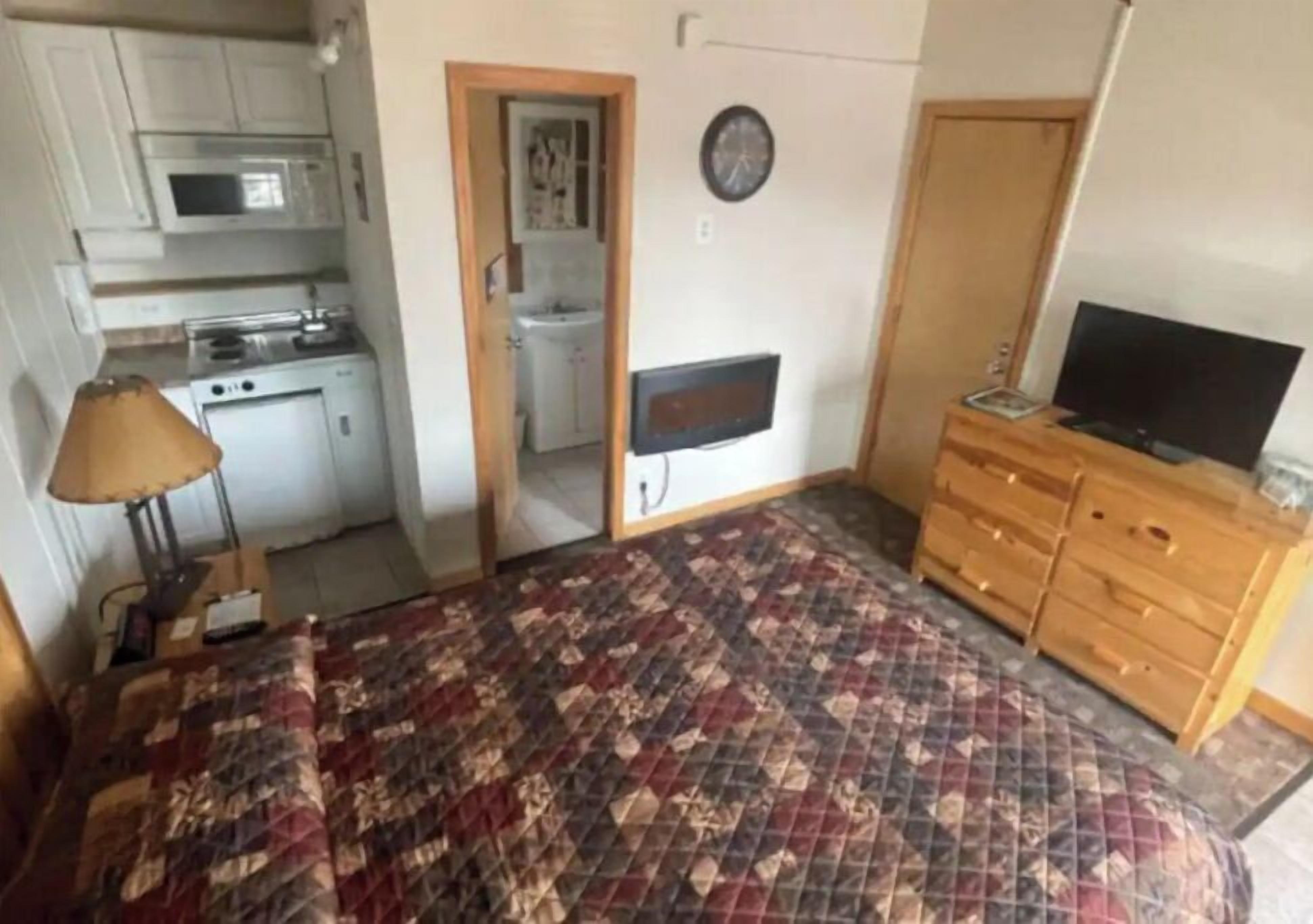 Une chambre comprenant un lit, une commode en bois, un téléviseur et une kitchenette équipée d’un four à micro-ondes et d’une cuisinière.