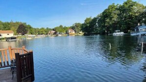 Ein ruhiger See mit einer hölzernen Anlegestelle, die sich ins Wasser erstreckt, umgeben von Häusern und Bäumen.