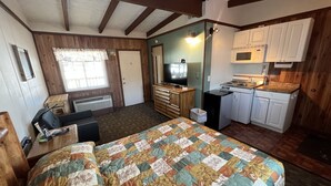 Une chambre de taille modeste comprenant un lit, un petit coin cuisine, une télévision et une fenêtre avec des stores.