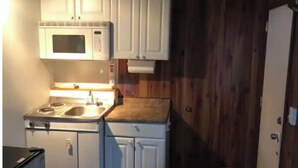 Une cuisine de taille réduite avec des meubles blancs, un four à micro-ondes, une cuisinière et un évier.