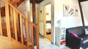 A wooden staircase leading to a bedroom with a bed and a nightstand. There is a black leather sofa with cushions and a small table with a lamp.