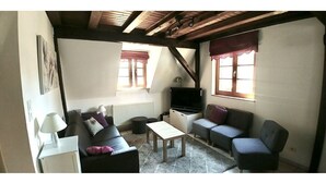 A cozy living room with a sofa, armchair, and a coffee table. There is a TV and a fireplace.