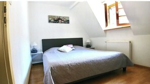 A bedroom with a bed, a nightstand, a lamp, a painting on the wall, and a window with a view of the outside.