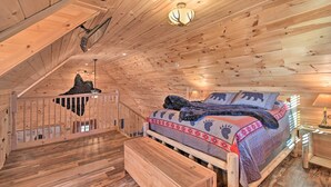 Ein gemütliches Schlafzimmer in einer Holzhütte mit Bett, Bank und einer Treppe zu einer erhöhten Ebene.