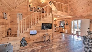 Ein Interieur einer Holzhütte mit Treppe, Fernseher, Kamin und Küchenzeile.