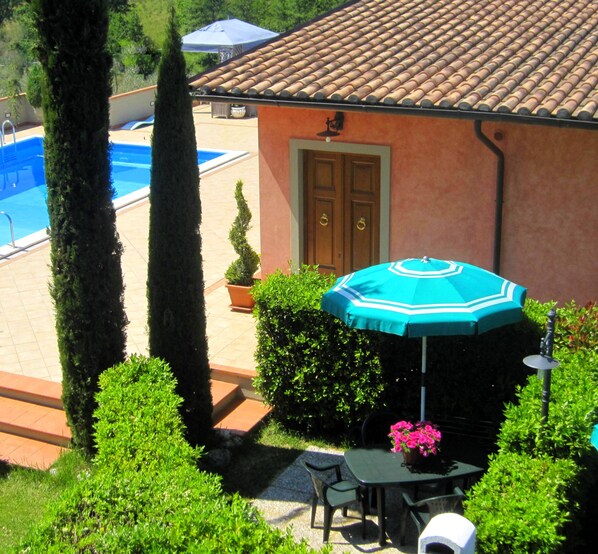 A patio with a table and chairs, a pool, and a building with a tiled roof.