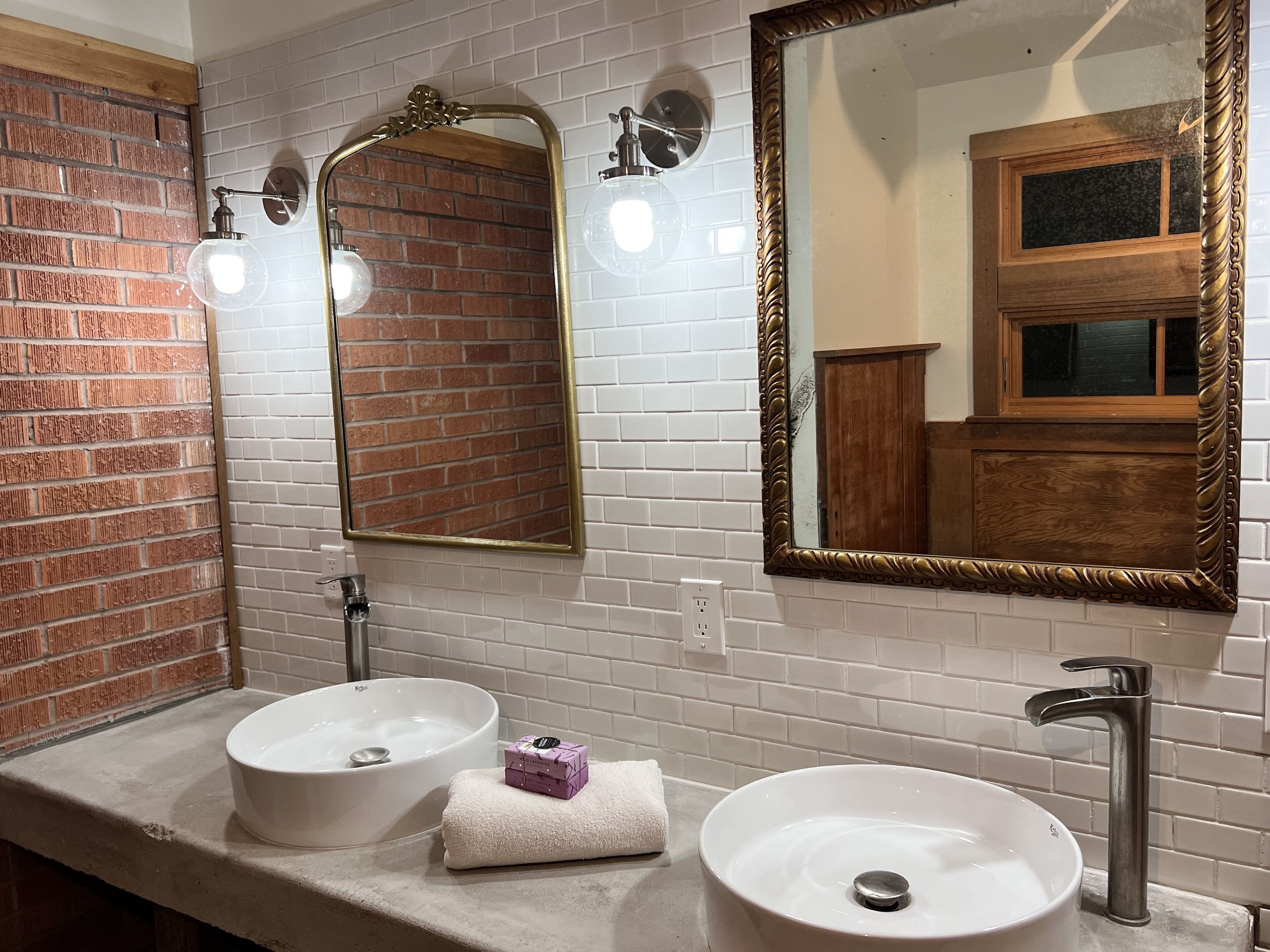 A bathroom with two sinks, a large mirror, and a brick wall.