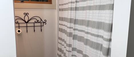 A small, narrow bathroom with a shower curtain, a toilet, and a window above the toilet.