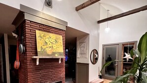 A living room with a brick fireplace, wooden flooring, a red stool, and a large potted plant. - Unique Cottage near Canyon Lands National Park (Monticello)